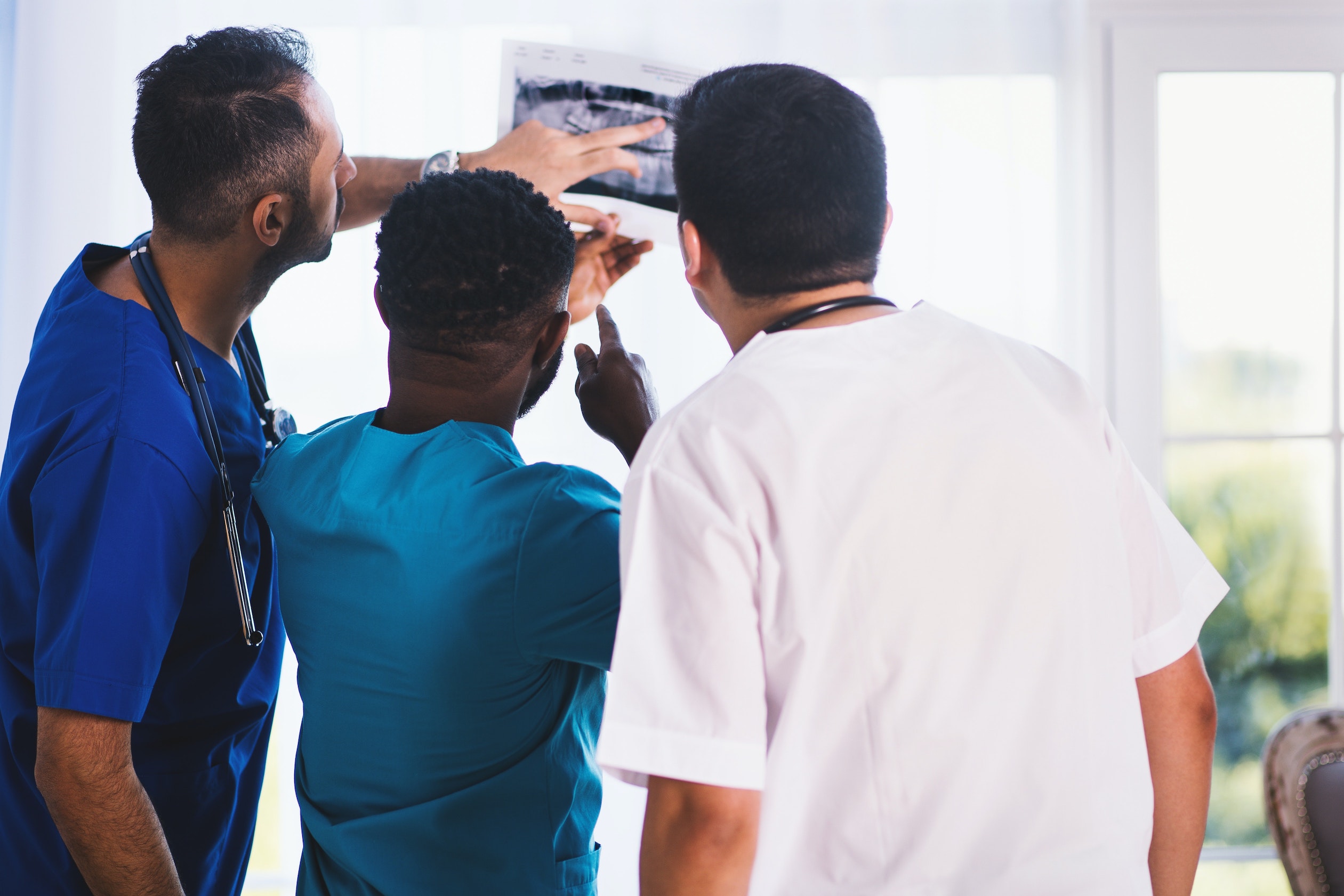Three Research Professionals CRO medical staff in blue scrubs review subject medical results in clinical setting.