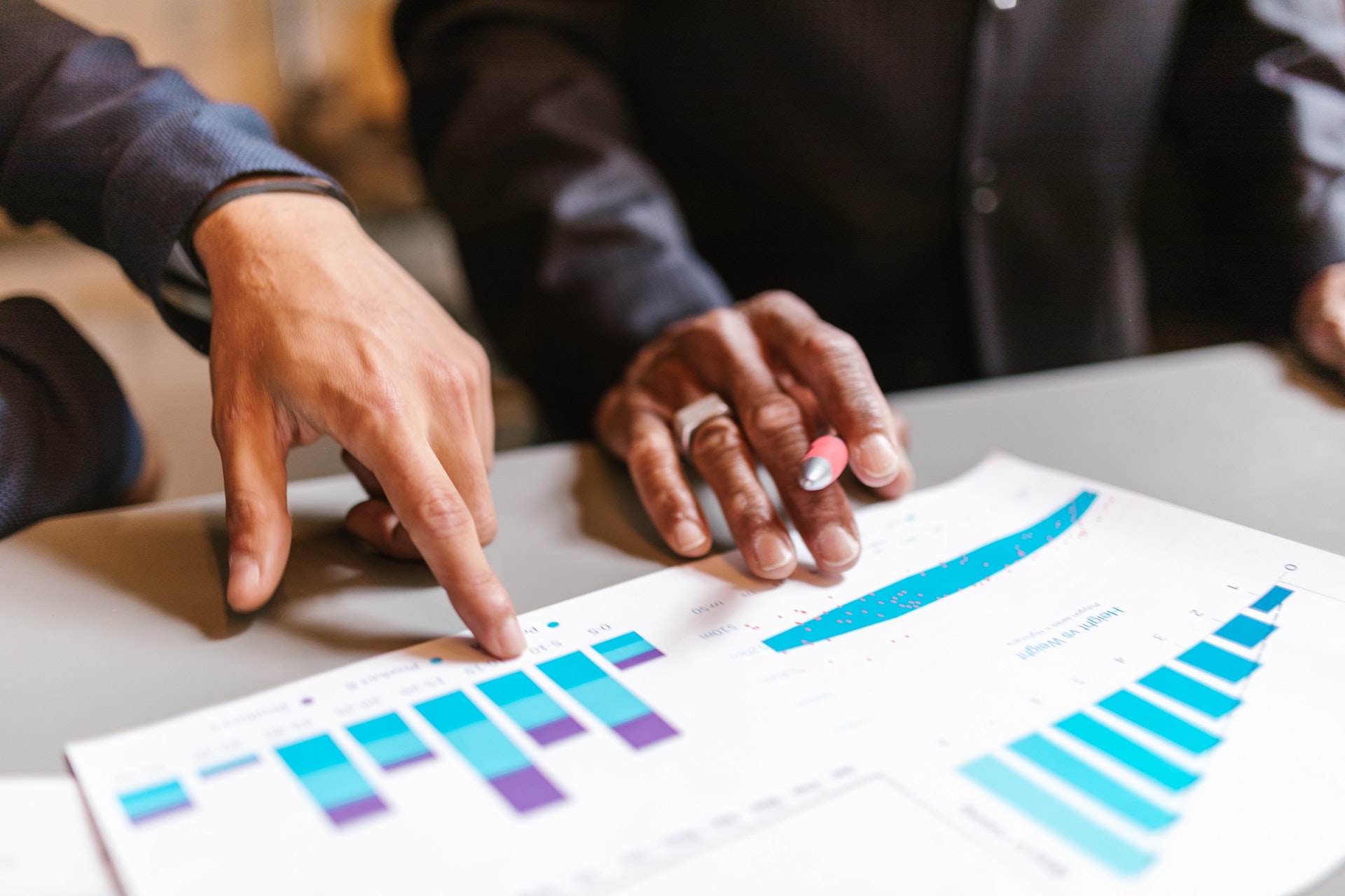 Two people's hands point to clinical trial data reports on paper on a desk at an RP-CRO clinical trial site.